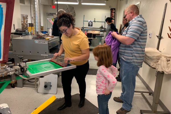 Young woman showing a little girl how to screen print.